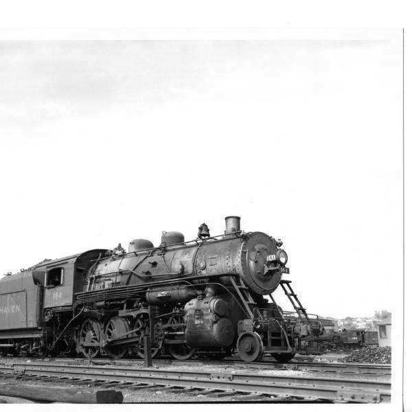 F-5 2-8-0 #163 (ex-CNE) backing onto turntable at Waterbury, CT roundhouse in late 1940's.  3/4 view: engineer's side front.  Tenders of #1007, 1027, 393, and 3003 visible in stalls.